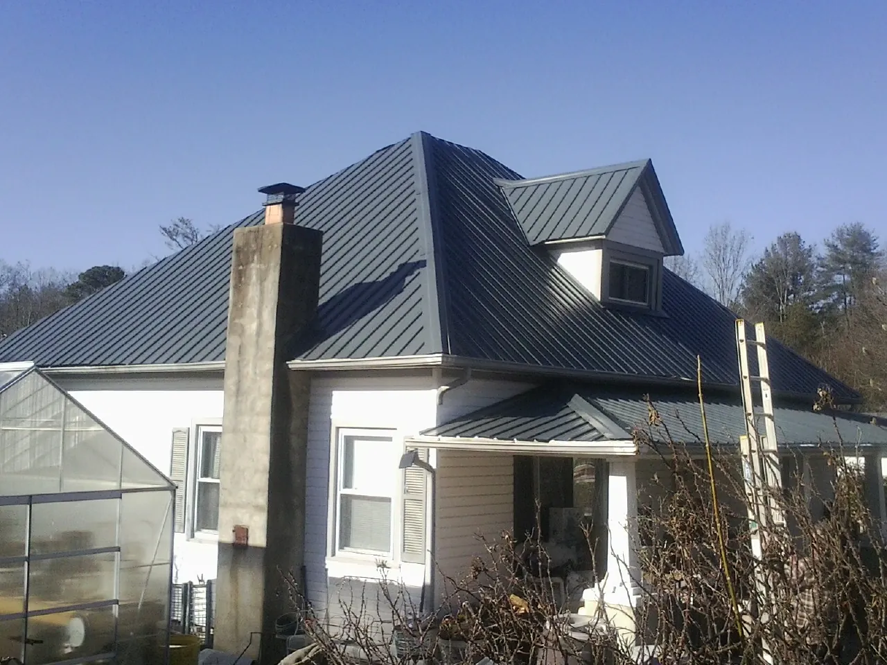 Dark blue standing seam metal roof on a white farmhouse with dormer — Slate & Tile Roof Repair by Roofing Brothers in Brooklet