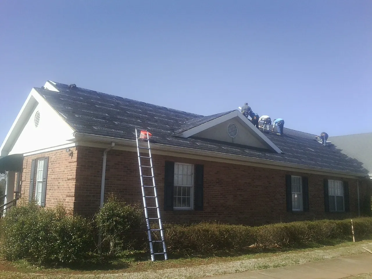 Crew tearing shingles off a brick ranch roof with a ladder set — Metal Roof Repair work by our crew in Brooklet