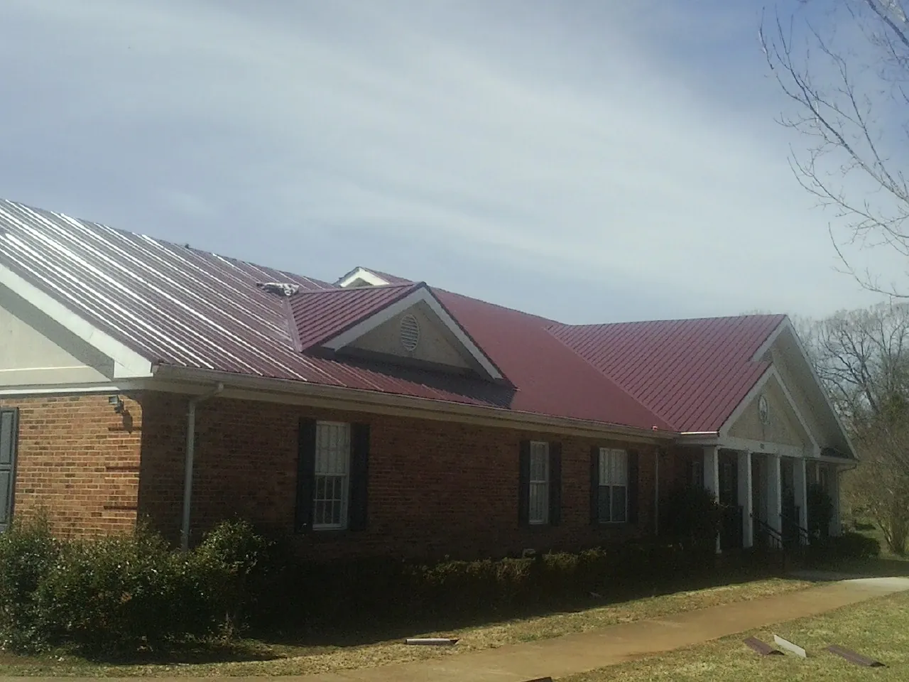 Red metal roof with gabled entries on a long brick building, from a Hail Damage Roof Repair job in Brooklet
