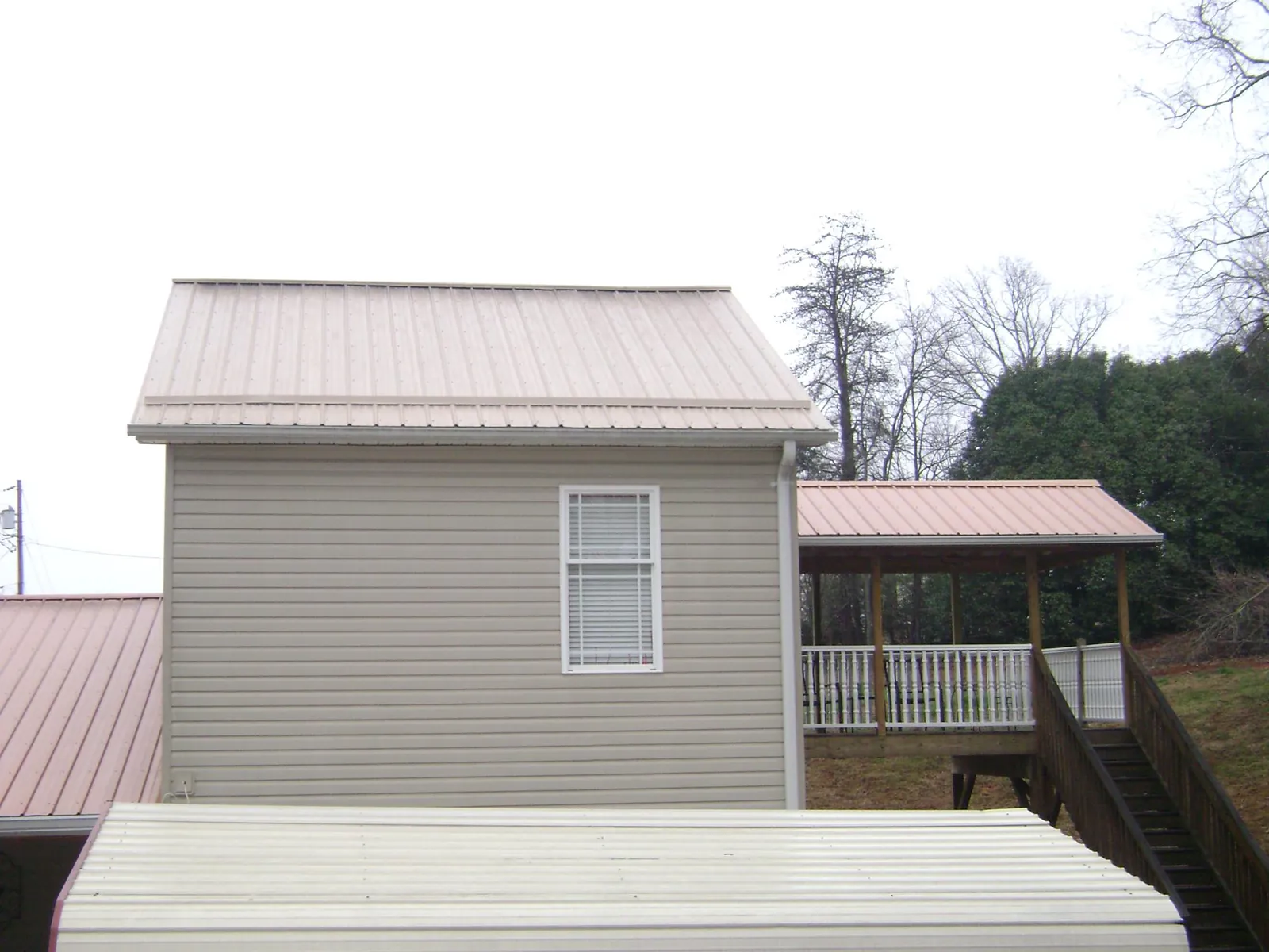 Tan metal roofs on a two story addition and attached porch, from a Roof Replacement job in Brooklet